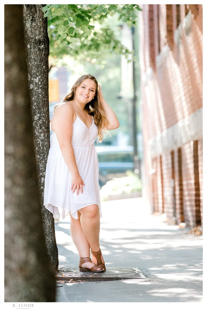 High school senior photo of a girl wearing a simple knee length white summer dress. 
