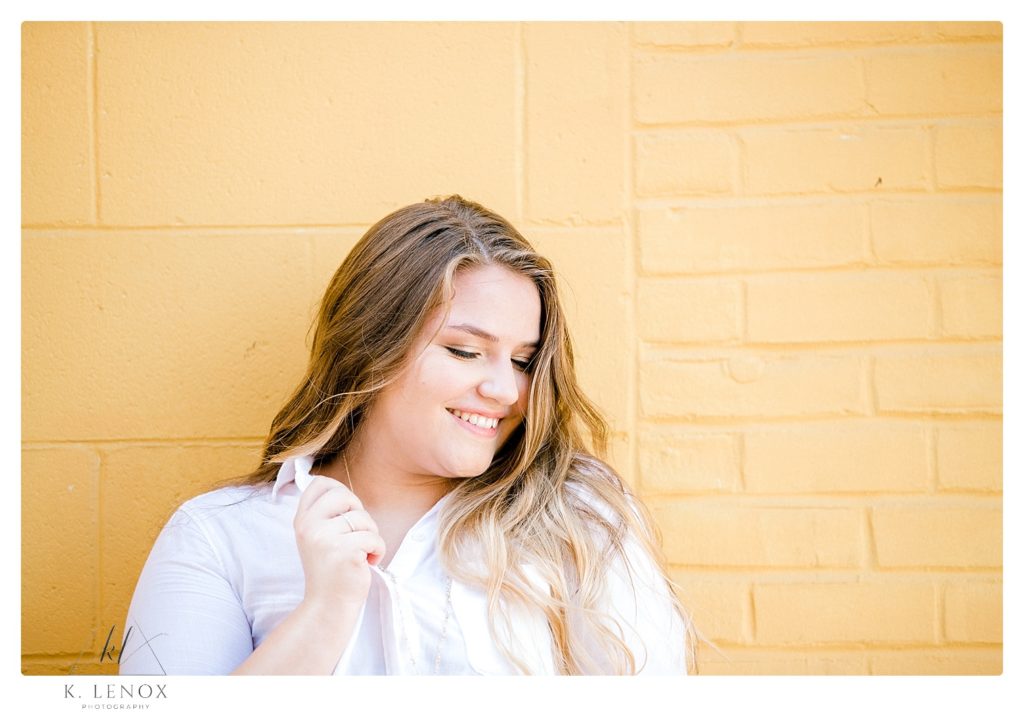 High School senior girl wearing a white button down t-shirt standing next too a yellow brick wall.  