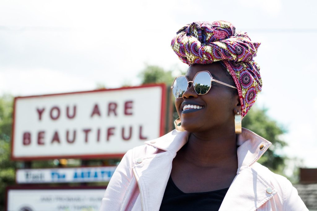 African American Woman stands in front of a sign that says" . You Are beautiful" Who's Perfect Anyway?