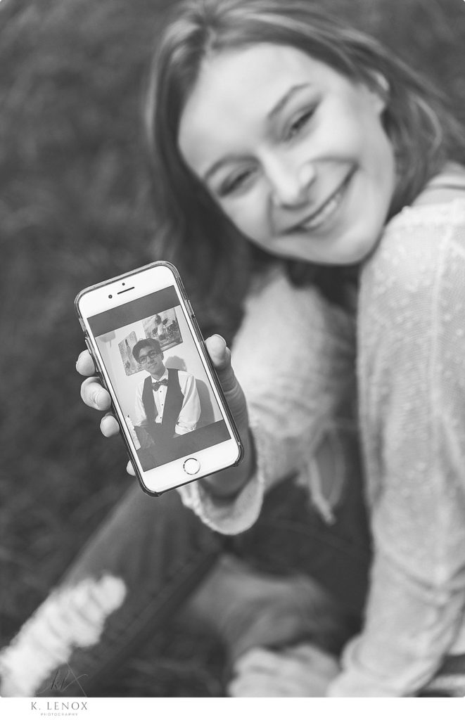 Black and white photo of a girl holding her phone up showing a picture of her boyfriend. 