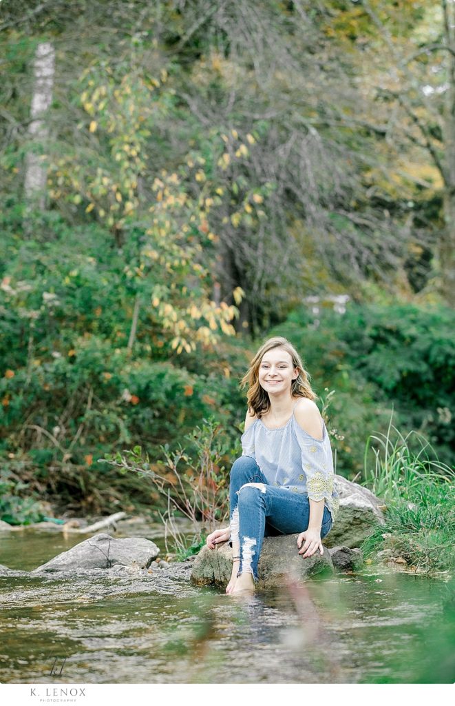 Light and Airy senior photo of a teenaged girl sitting on a rock wading her feet in the stream at Stonewall Farm. 