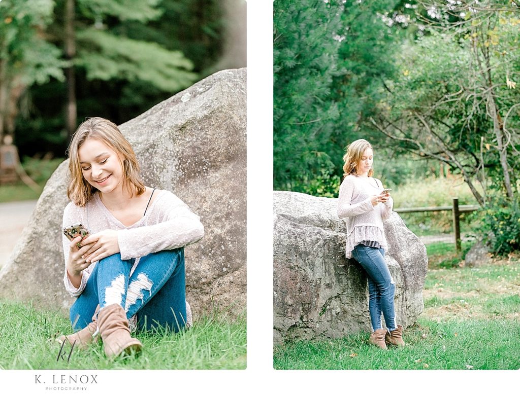 Highschool senior leaning against a big rock while playing with her cell phone. 