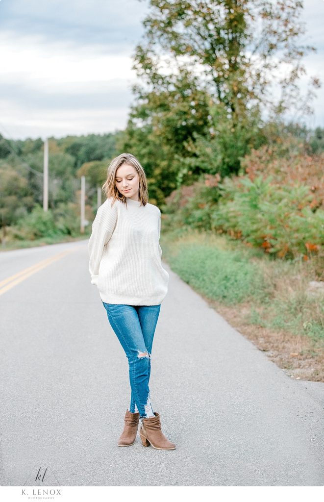 Light and Airy Senior photos of a girl wearing blue jeans and a white sweater- standing near Stonewall FArm. 