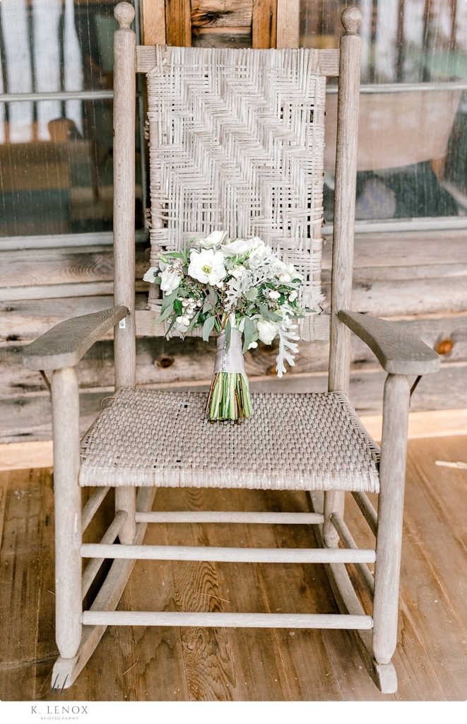 Rustic Wedding detail photo showing the white floral bridal bouquet in a light brown wicker rocking chair. 