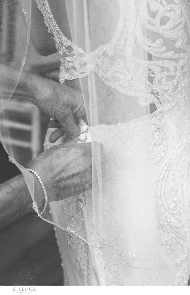 Black and White photo of a back of a brides dress as she is getting it buttoned. 