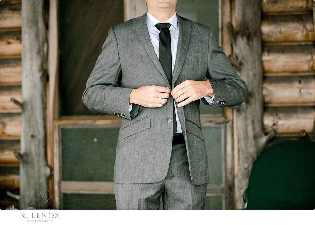 A groom buttoning his jacket on the porch of a rustic lakeside cabin. 