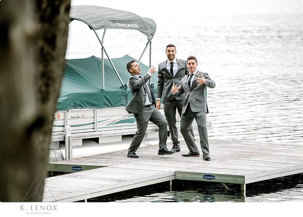 Candid photo of three men in grey suits hanging out lakeside on a dock. 