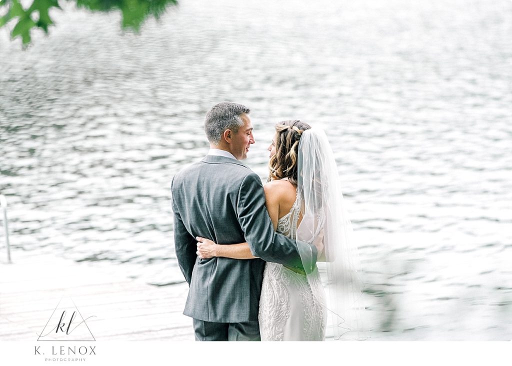 Bride and groom stand with their arms around each other while looking out over the lake at Camp Takodah Wedding. 