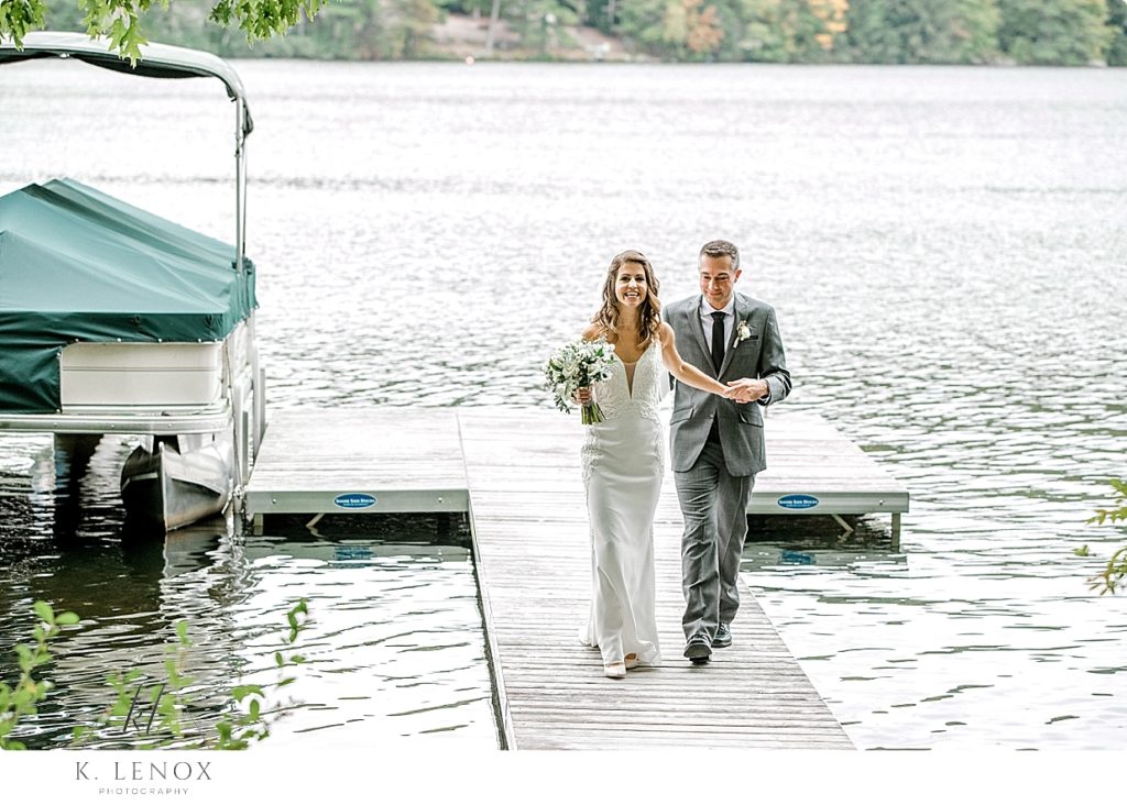 Groom helps his bride walk on the dock on their wedding day. 