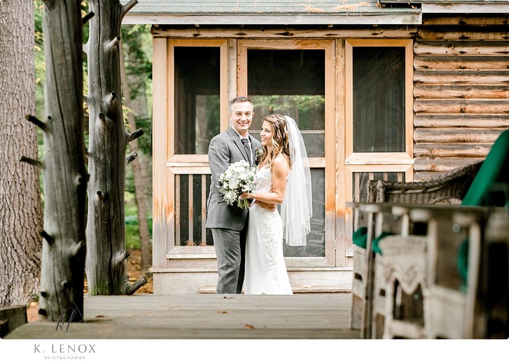 Bride and Groom holding each other while showing parts of the rustic lakeside cabin porch. 