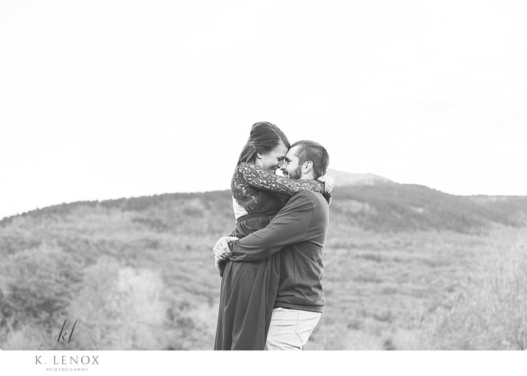 Black and white photo of a man picking up his fiance during their engagement session by Mount Monadnock. 