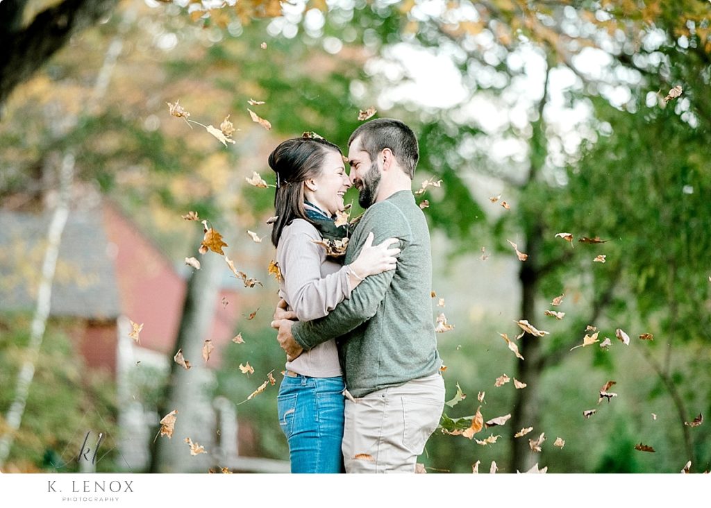 Light and Airy photo of a man and woman hugging while leaves fall around them. Fall Engagement Session in NH. 