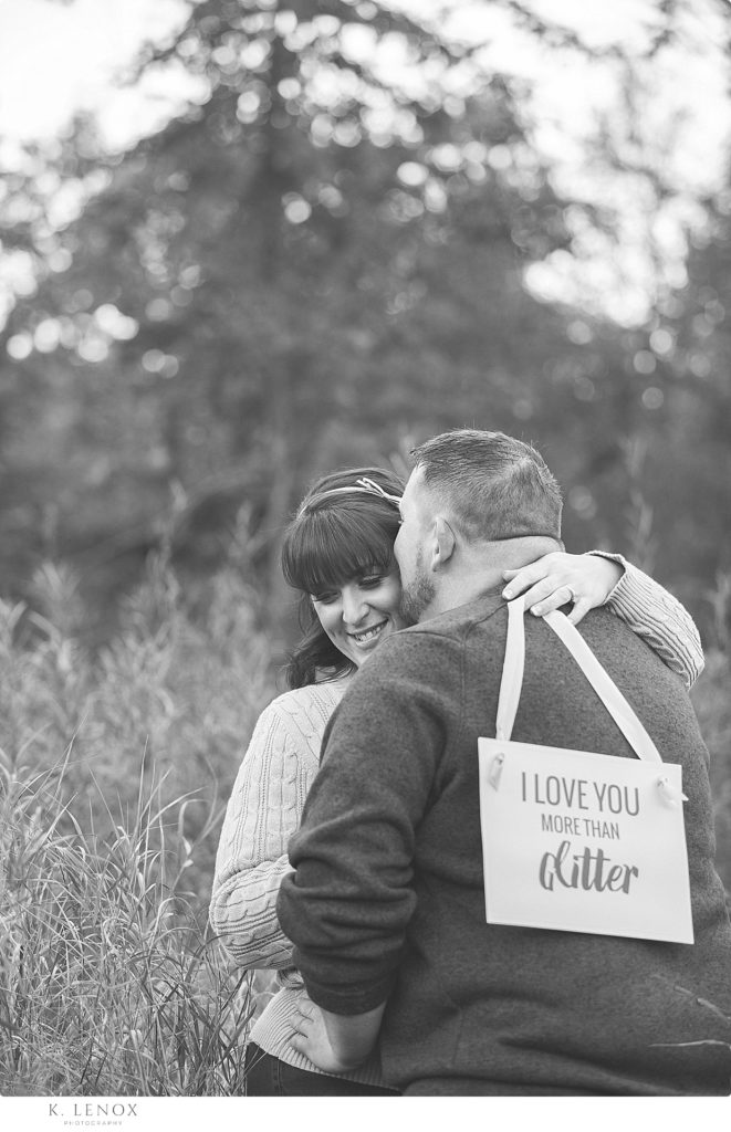 Black and white photo of a man and woman holding a sign that says. . "I love you more than glitter" 