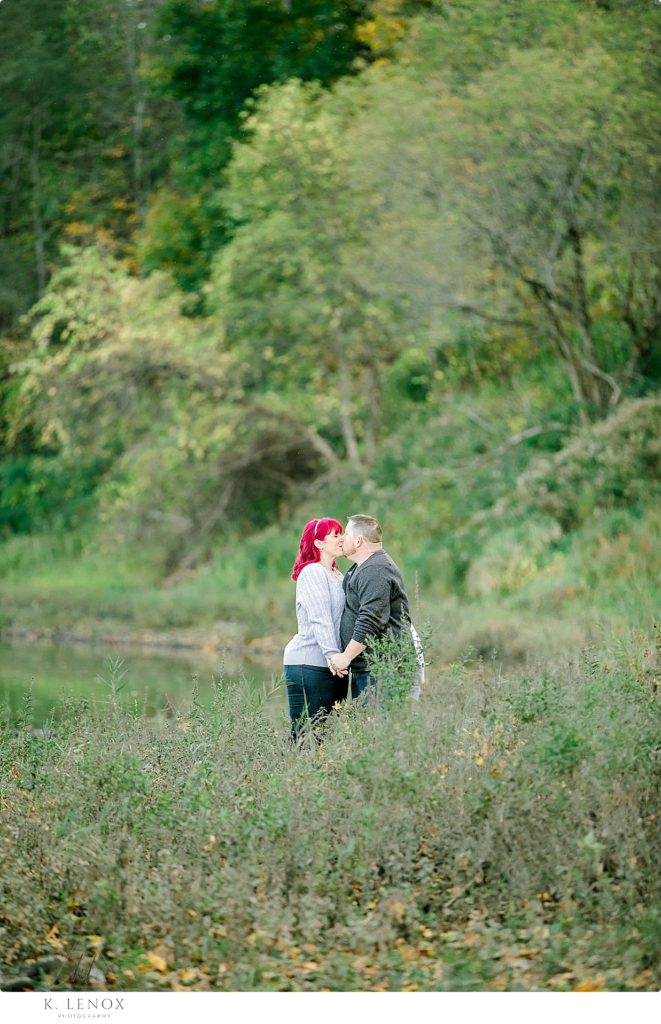 Man and Woman kiss while surrounded by trees and grass while on their engagement session in VT. 
