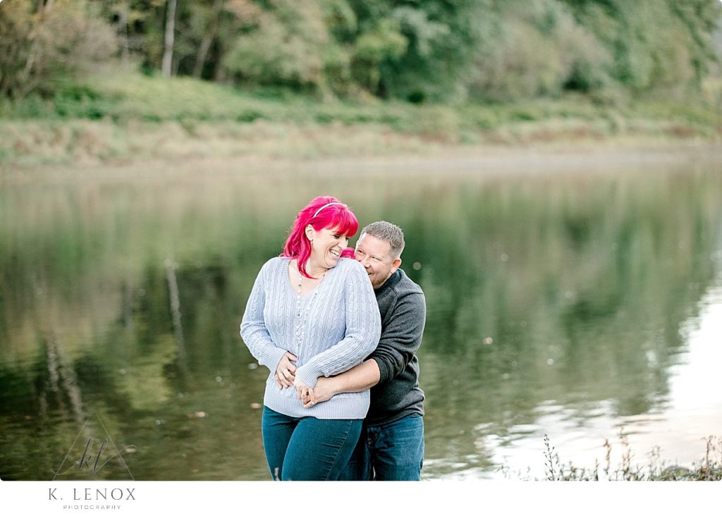 Man and Woman giggle and laugh at the bank of a river in VT. during their engagement session. 