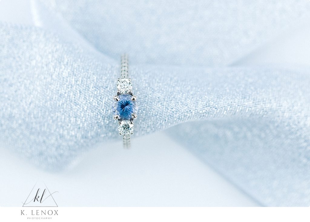 White gold engagement ring with blue stone surrounded by two diamonds. 