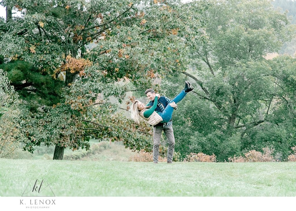 Light and Airy photo showing a Man scooping up his fiance while at their engagement session on Scott Farm. 