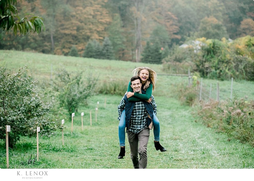 Engaged Couple take a piggy back ride in the Orchard at Scott Farm during their fall engagement session. 