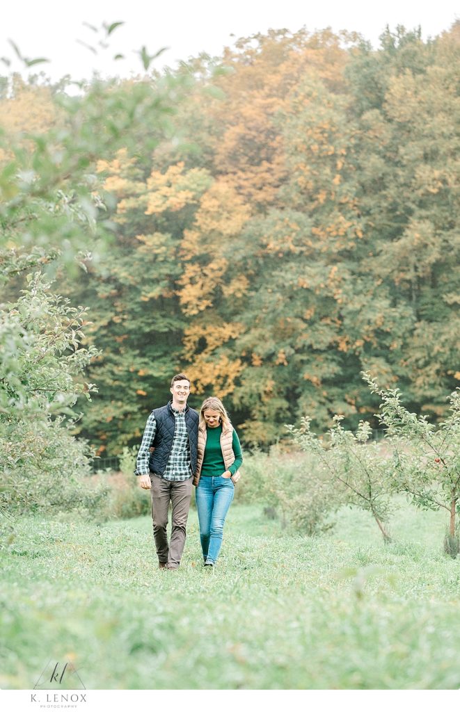 Engaged couple walk holding hands in the Orchard at Scott Farm during their fall photo session. 