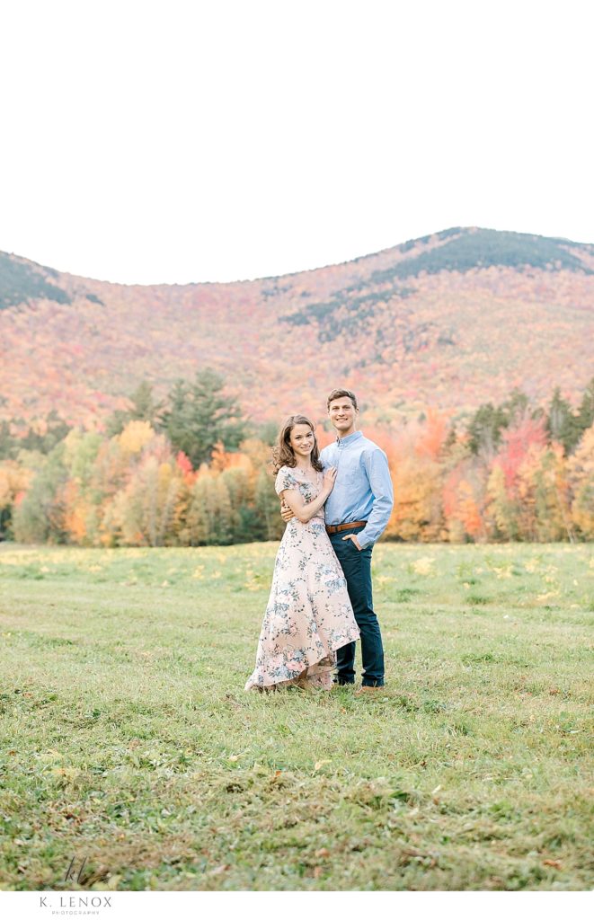 Light and Airy Engagement Photos in the White Mountains of NH- Man and Woman pose in front of a mountain with the fall foliage in the background. 