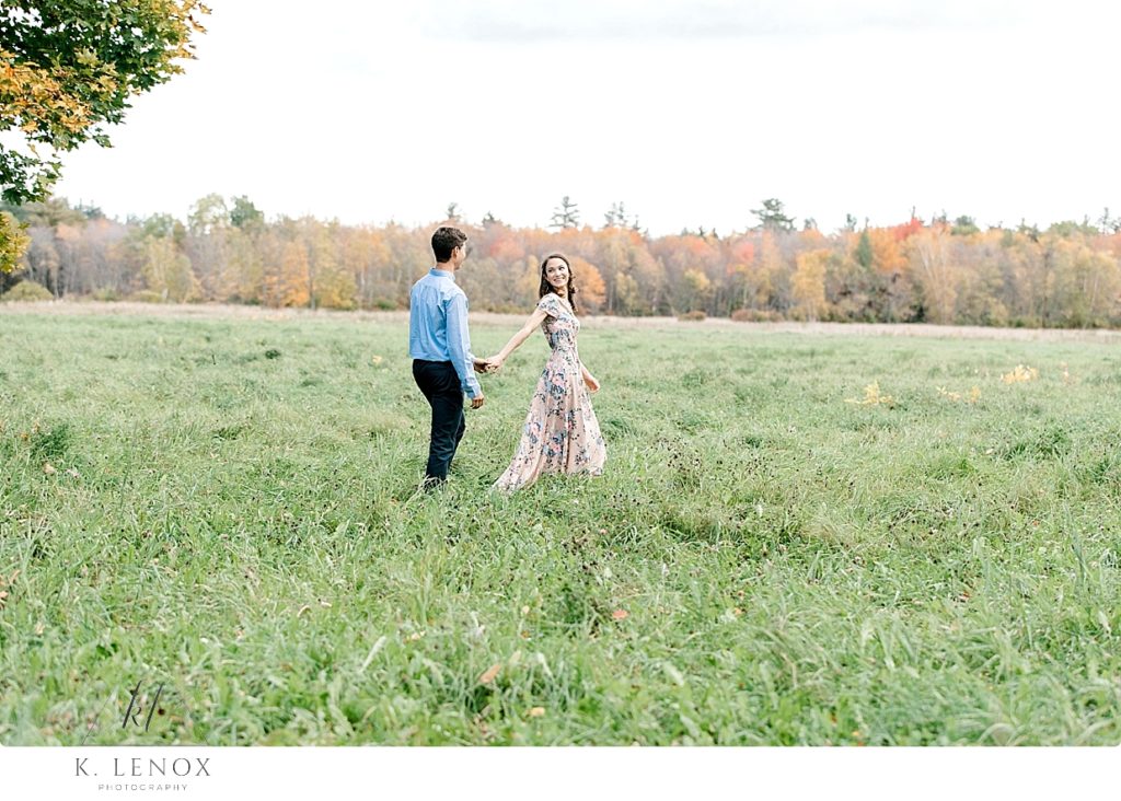 Man and woman walk holding hands in a field for their Light and Airy Engagement Photos in the White Mountains of NH