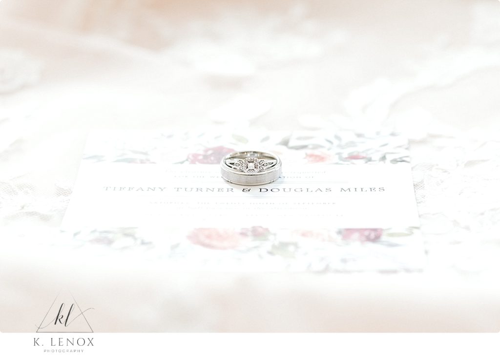 White gold antique looking engagement ring and wedding band photographed over a white wedding invitation. 