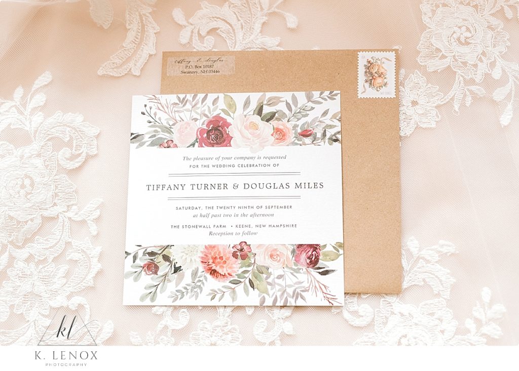 Simple white and floral wedding invitation with a Kraft envelope laying over lace. 