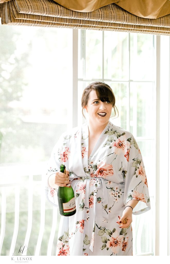 Bride wearing a light floral robe holds bottle of champagne. 