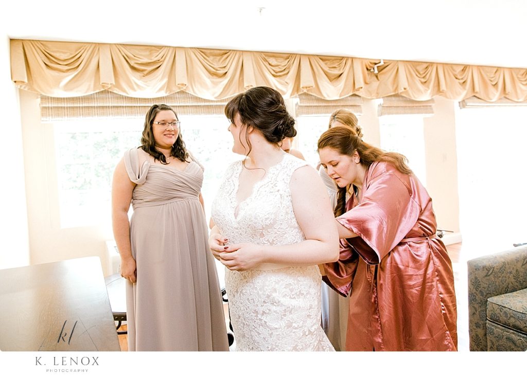 Bridesmaids help the bride into her lace dress. 