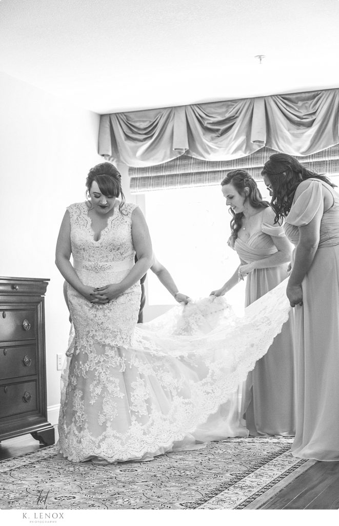 Black and white photo of bridesmaids helping a bride straighten her dress. 