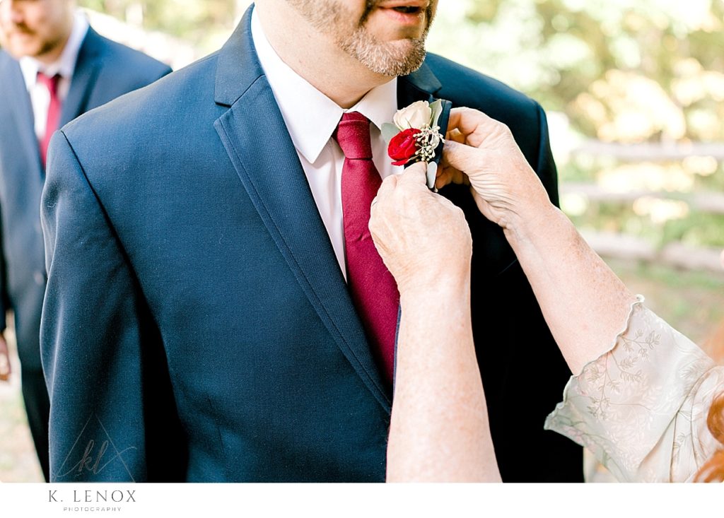 Groom's mom puts on his boutonniere with a red and white flower. 