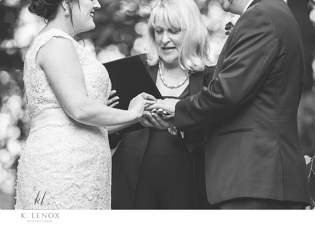 Black and White photo of the bride and groom exchanging rings during the wedding ceremony at stonewall farm. 