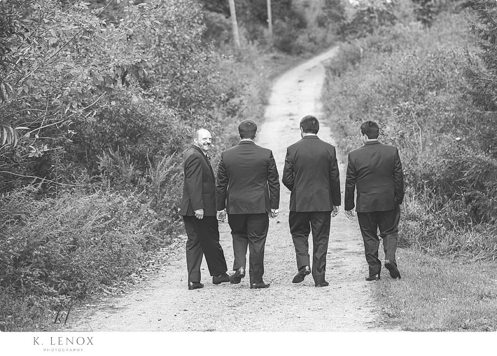 Black and White photo of a Groom and his three groomsmen walking away on a dirt path at Stonewall Farm. 