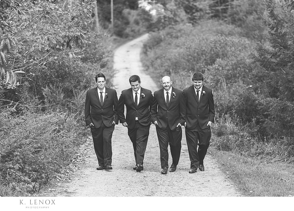 Black and white image of a groom and his groomsmen walking on a dirt road. 