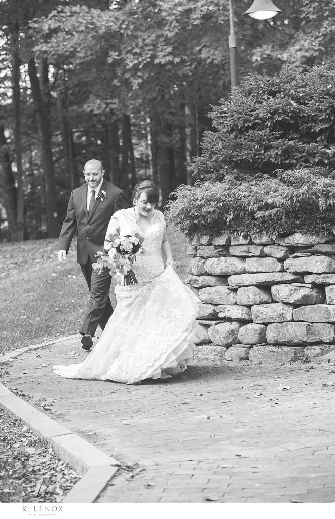 Black and white photo of a Bride and Groom walking near a stone wall at Stonewall Farm. 
