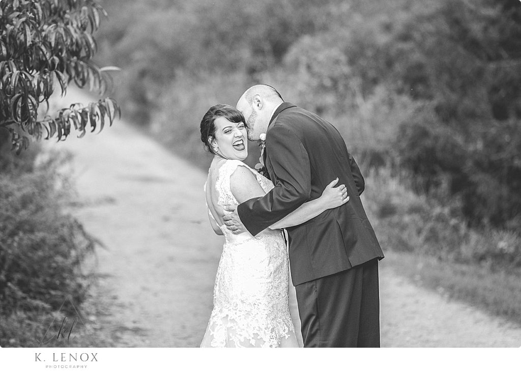 Black and white photo of a bride laughing at something her groom is whispering in her ear. 