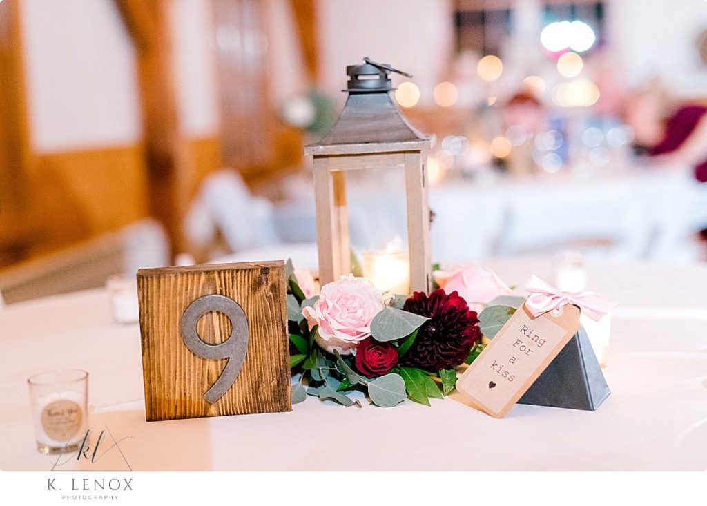 Wedding Reception Centerpieces. Lanterns with lit candles surrounded by florals and wooden table numbers. 