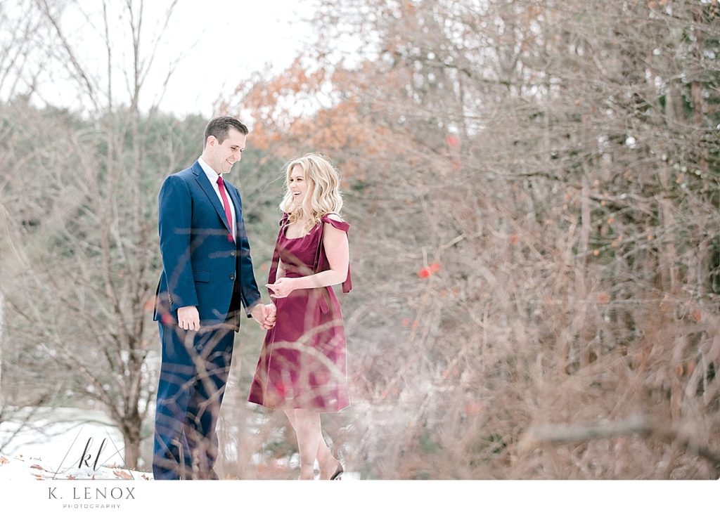 Candid photo of a man and woman laughing during their engagement session wearing a Maroon Christian Siriano Dress and Black Christian Louboutin heels. 