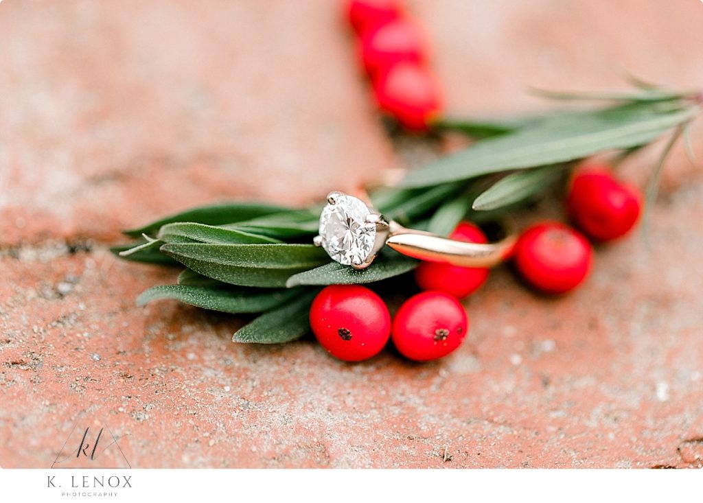 White gold engagement ring shown with red berries and green leaves. 