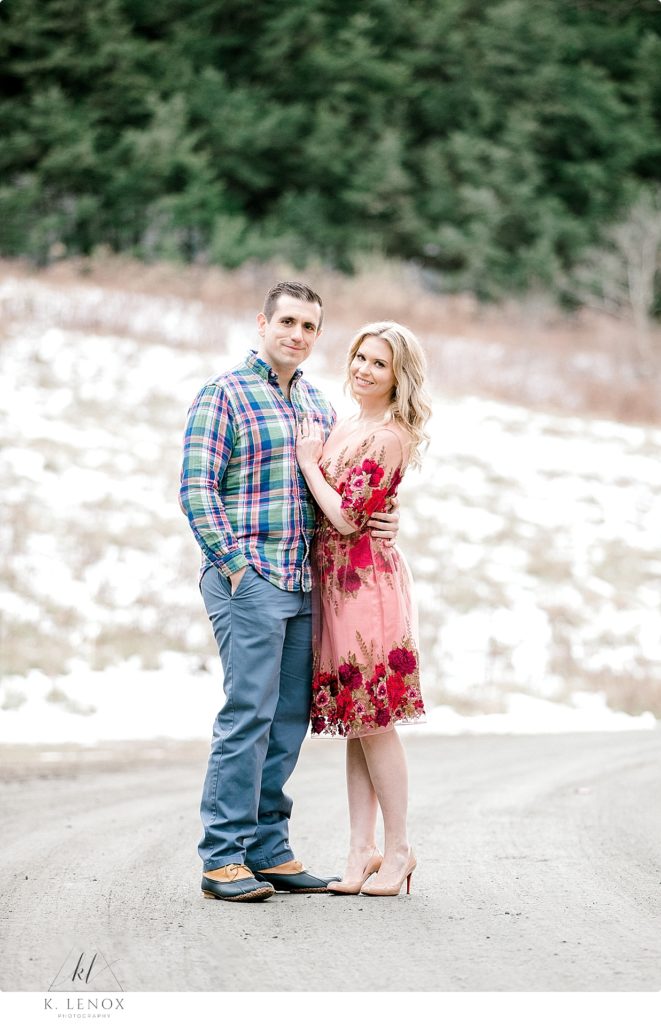 Man wearing blue/green and pink plaid shirt poses with a woman wearing a red floral dress-
