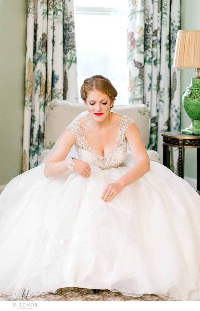 Beautiful Red headed bride w/ red lipstick sits in her beaded wedding gown in the bridal suite of the Omni Mount Washington Resort. 