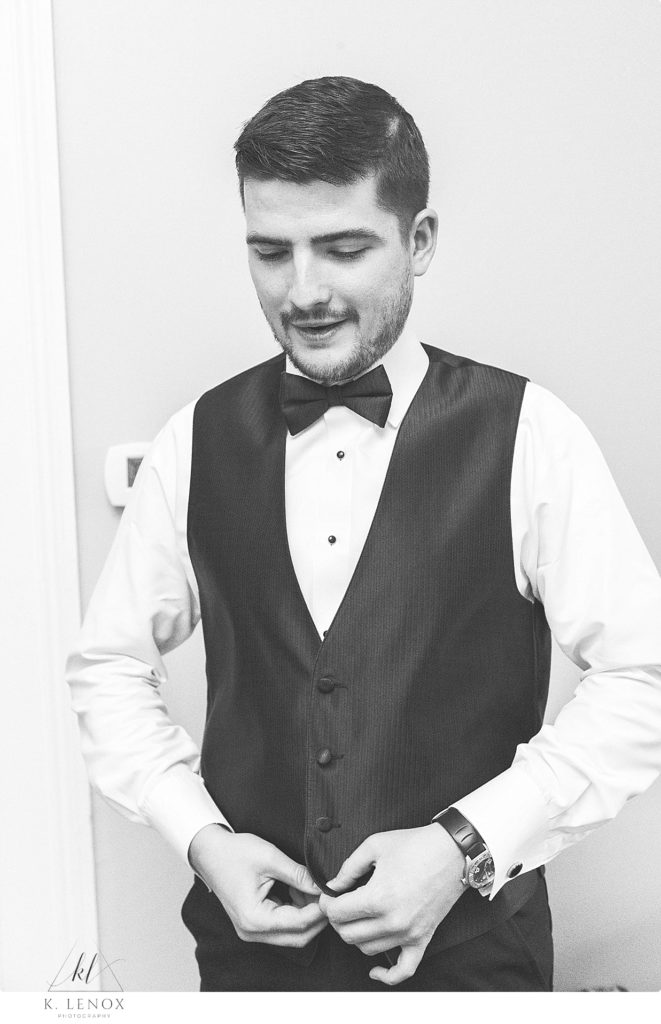 Black and White photo of a groom buttoning the vest to his tux on his wedding day. 