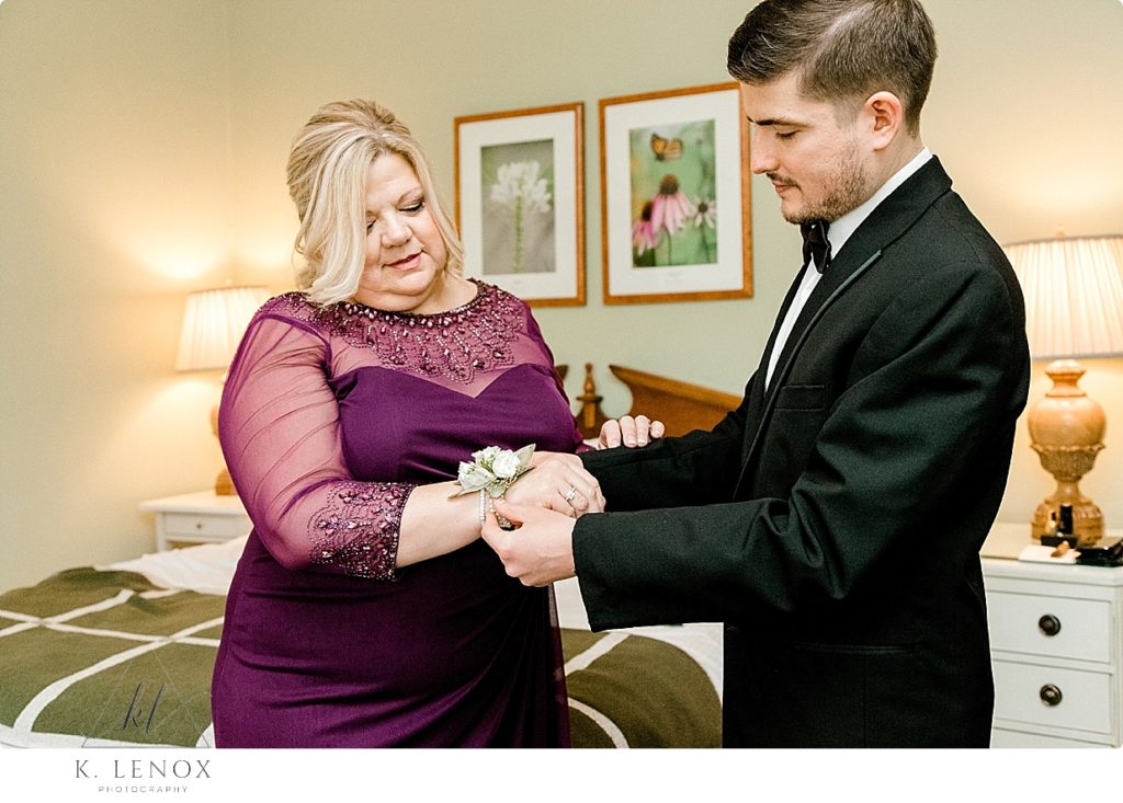Mother wearing purple dress gets her corsage put on by her son the groom for their Winter Wedding. 