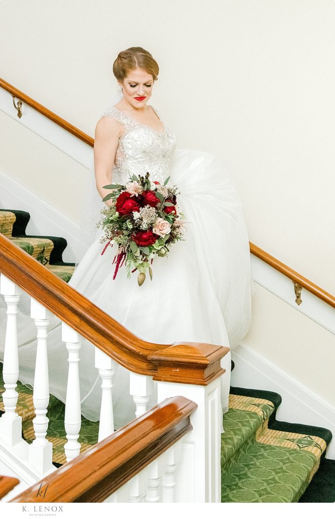 Beautiful bride walks down the stairs holding her bridal bouquet for her Christmas Wedding at the Omni Mount Washington Resort. 