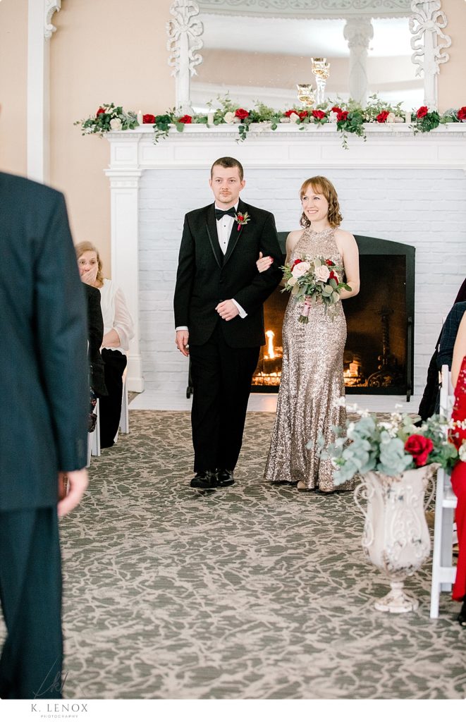 Wedding Attendants walk down the aisle for a Christmas wedding. Bridesmaid wearing a gold sequin dress and a man wearing a black tux. 