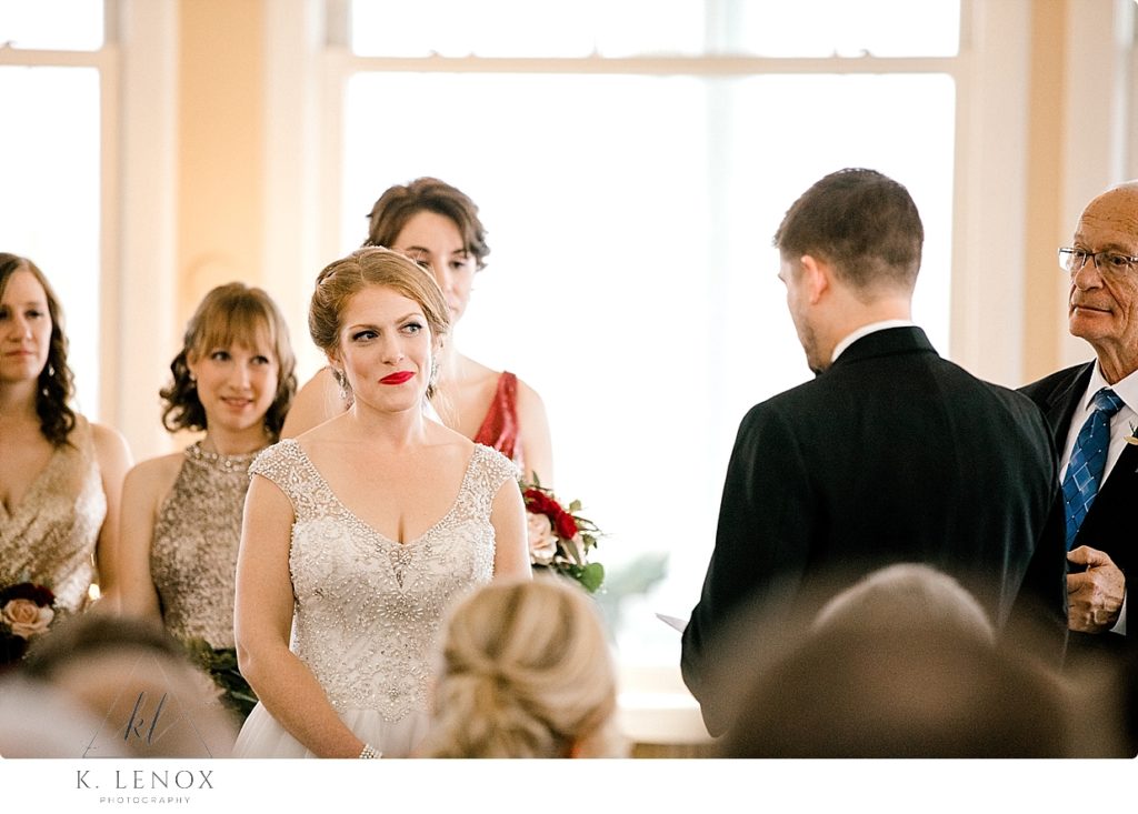 Bride with red hair and red lipstick lovingly smiles at her groom during their wedding ceremony. 