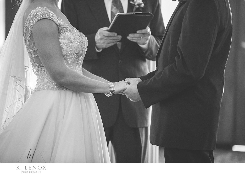 Black and White photo of a bride and groom holding hands during their wedding ceremony. 