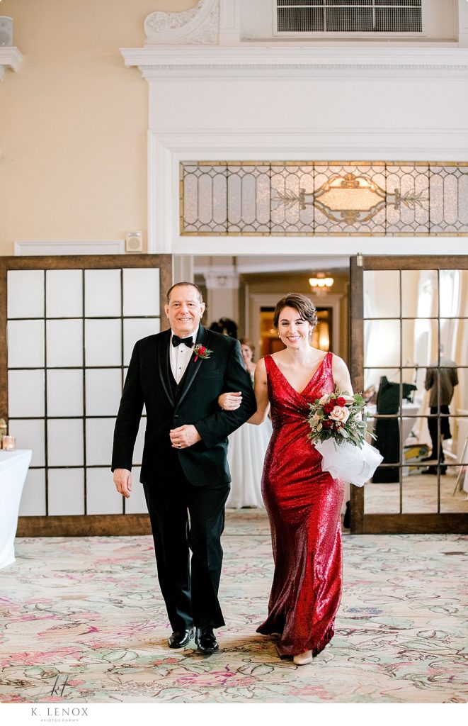 Maid of honor wearing a red sequin dress and the best man wearing a tux, get introduced into the Sun Dining room Christmas wedding Reception