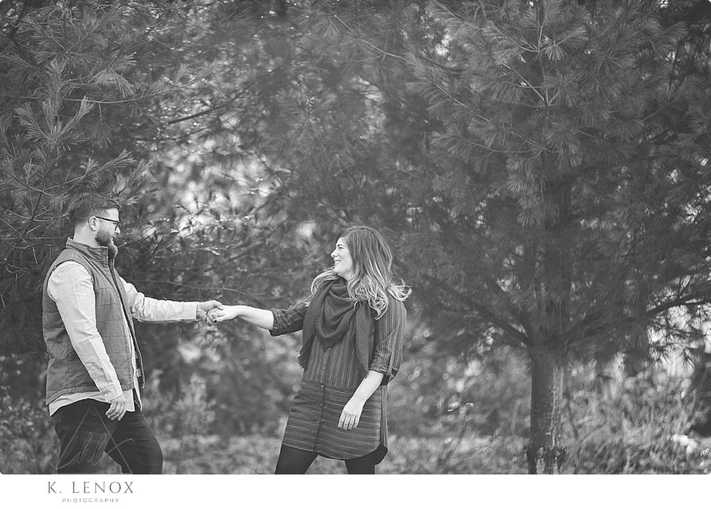 Candid black and white photo of an engaged couple holding hands and laughing. 