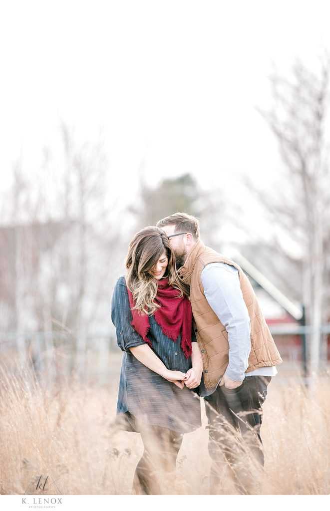 Candid engagement photo of a man and woman wearing a navy blue shirt dress and a red scarf. 